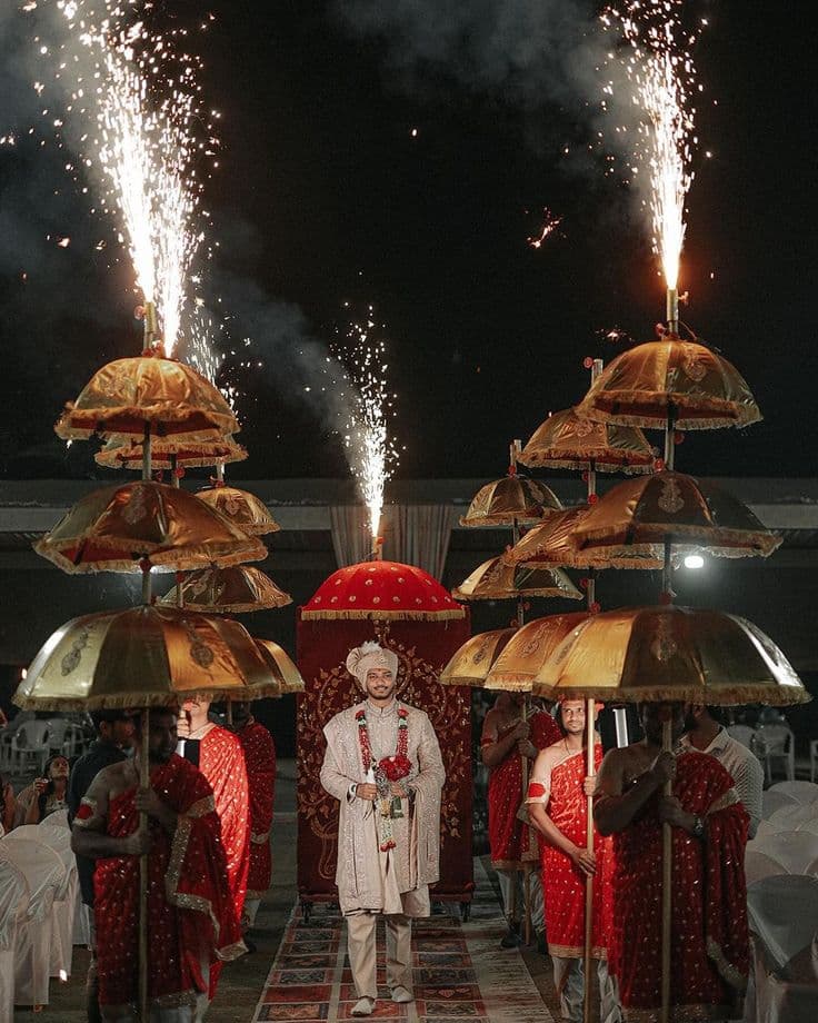 Groom making a grand Baraat entrance beneath ceremonial umbrellas and pyrotechnics